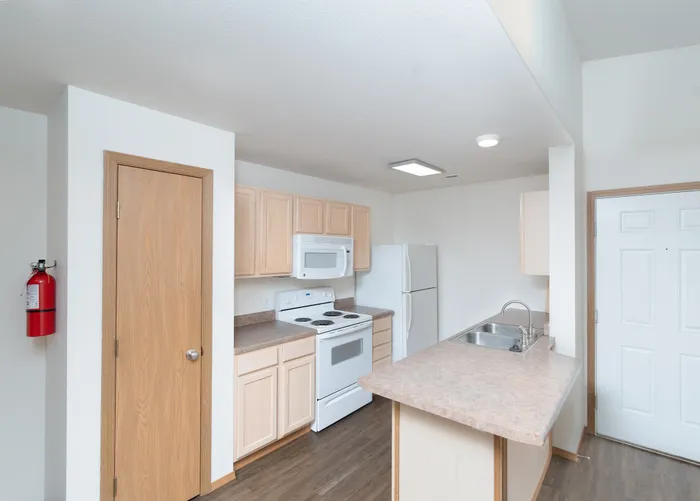Bright, modern kitchen with light wood cabinetry, sleek countertops, all-white appliances, and a convenient breakfast bar.