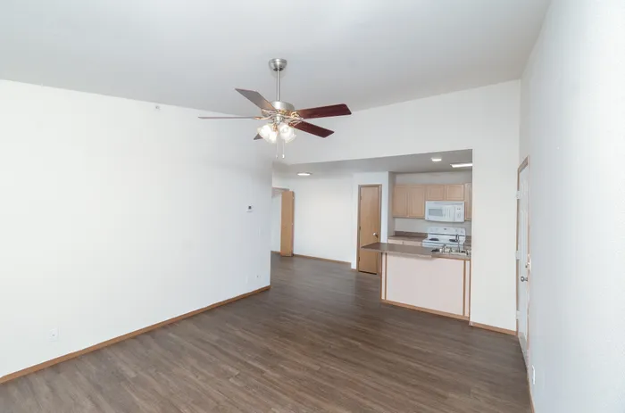 Modern open-concept apartment with wood flooring, featuring a ceiling fan and a stylish kitchen with light wood cabinetry.