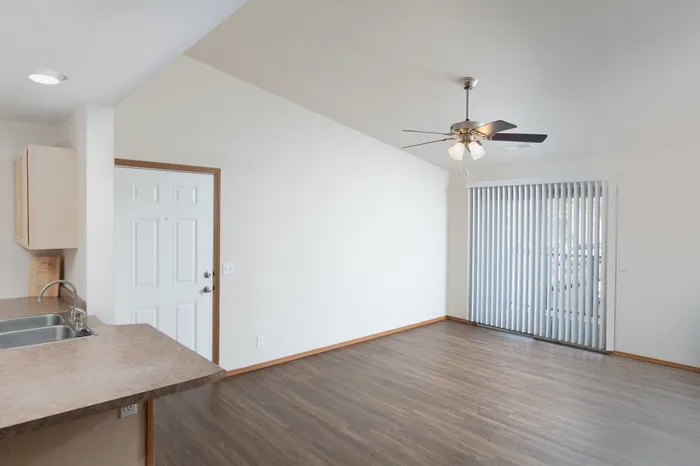 Bright and airy open-plan interior featuring a sleek kitchen counter, modern ceiling fan, and elegant hardwood flooring with expansive glass doors.
