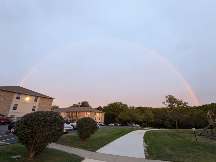 Charming apartment complex under a stunning rainbow, with lush greenery and inviting pathways.