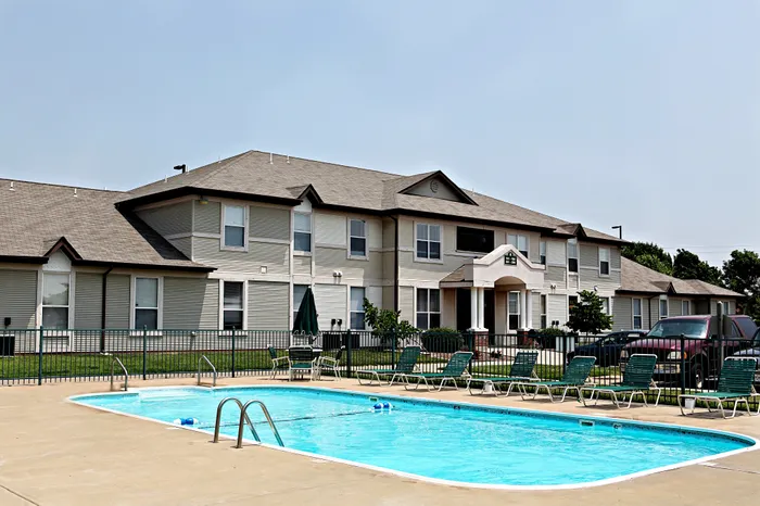 Outdoor swimming pool at Chesterfield Village with concrete deck, lounge chairs, and gated fencing, located in front of a two-story apartment building.