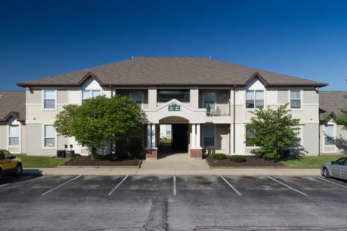 Two-story Chesterfield Village apartment building with beige siding, brown rooflines, covered central entry, and landscaped walkways under a clear blue sky.