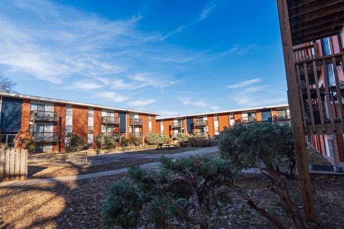 Courtyard view at Seminole North Apartments with multiple two-story brick buildings, private balconies, paved walkways, landscaped shrubs, and a picnic table in a central green space.