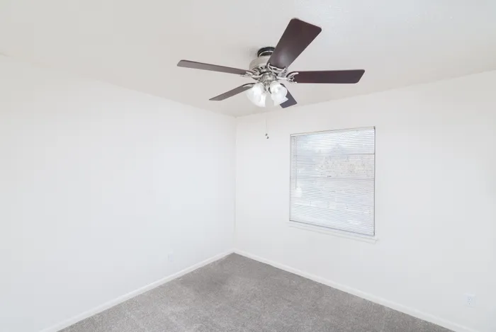 Bright room with modern ceiling fan, plush carpet, and large window offering natural light.