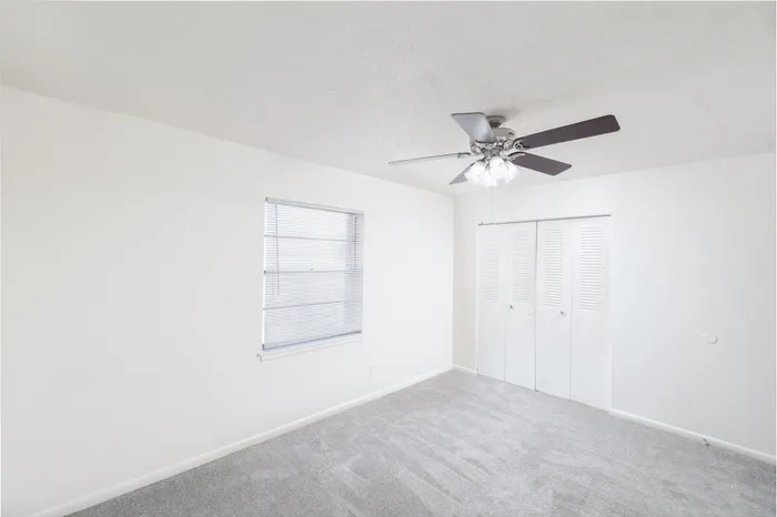 Bright, modern room with plush carpeting, sleek ceiling fan, and ample closet space for a cozy, inviting atmosphere.