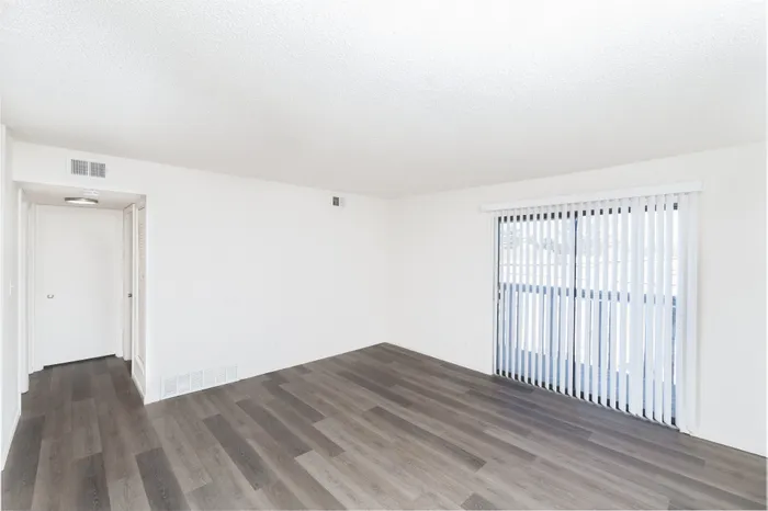 Bright and spacious living area with sleek wooden flooring and large sliding glass doors for abundant natural light.