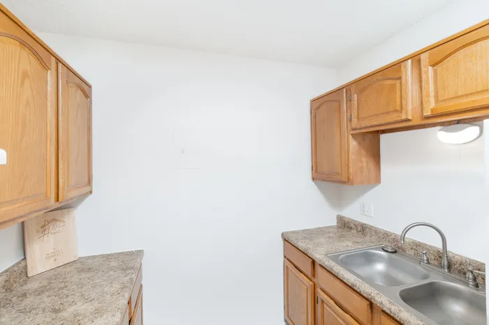 Galley-style kitchen featuring wood cabinets, double-basin stainless steel sink, laminate countertops, and overhead lighting at Seminole North Apartments.