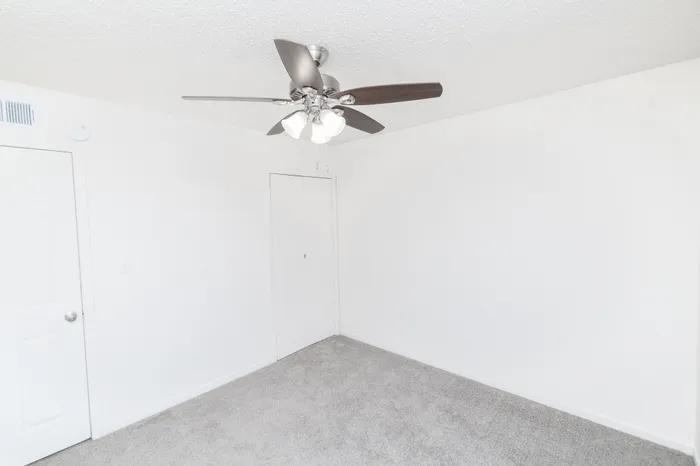 Carpeted bedroom with white walls, a ceiling fan with overhead light, and a single door, offering a clean and simple layout at Seminole North Apartments.