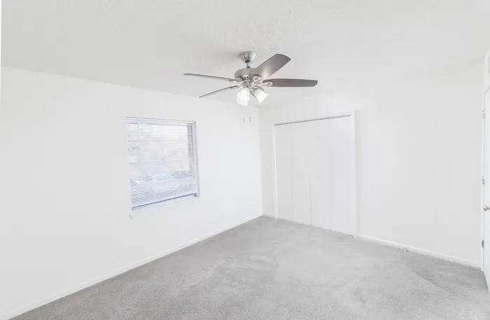 Bedroom featuring soft carpet, white walls, a ceiling fan with light, window with blinds, and a double-door closet at Seminole North Apartments.