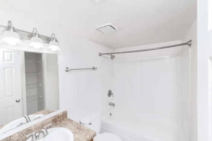 Bathroom with laminate countertop vanity, sink, mirror, overhead lighting, toilet, and tub-shower combination with curtain rod at Seminole North Apartments.