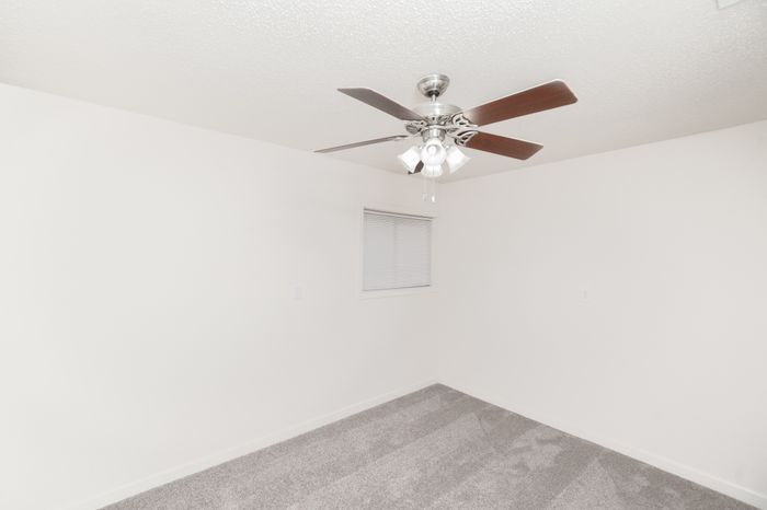 Bright, minimalist bedroom with plush carpet and modern ceiling fan, perfect for a cozy retreat.