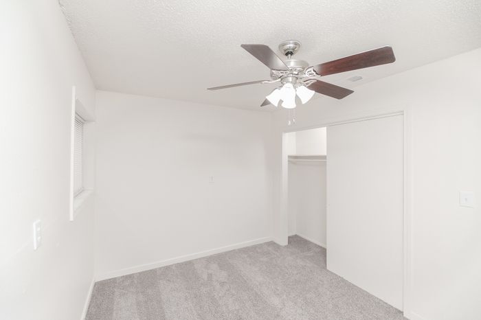 Bright, cozy white bedroom with modern ceiling fan and spacious closet, ideal for personalization.
