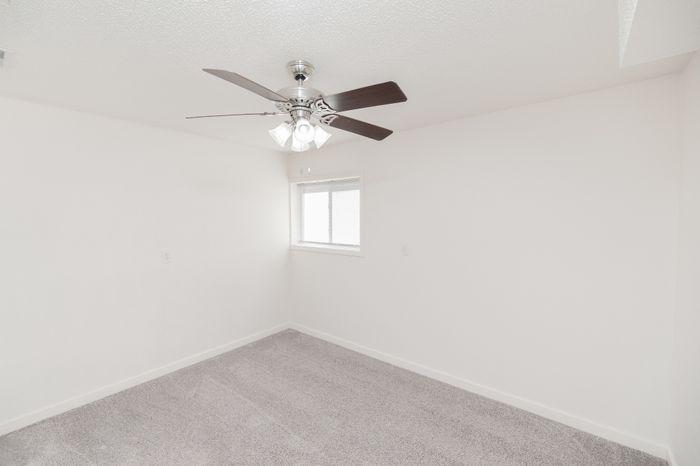 Bright and inviting bedroom with plush carpet and modern ceiling fan, perfect for relaxation.