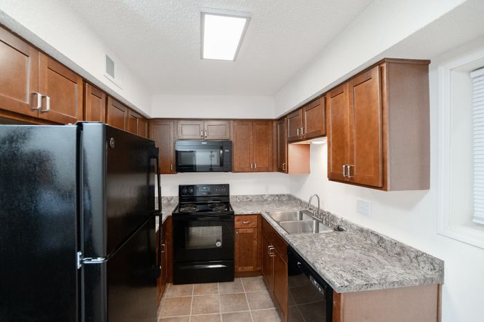 Updated kitchen featuring wood cabinets, black refrigerator, stove, microwave, dishwasher, gray countertops, tiled floor, and overhead lighting.