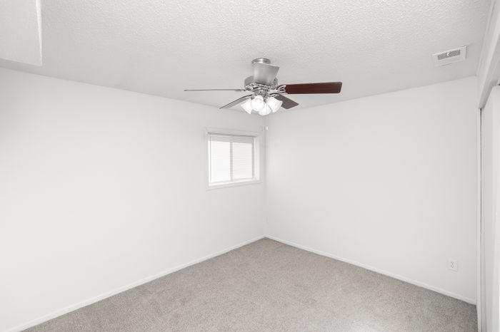 Secondary bedroom with carpeted floor, white walls, ceiling fan with light, and a small window with blinds.