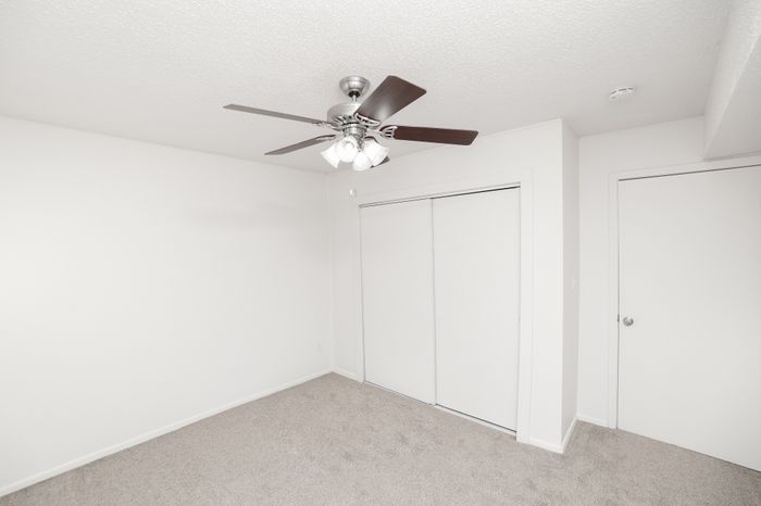 Bedroom featuring carpeted flooring, ceiling fan with light, sliding closet doors, and adjacent hallway door.