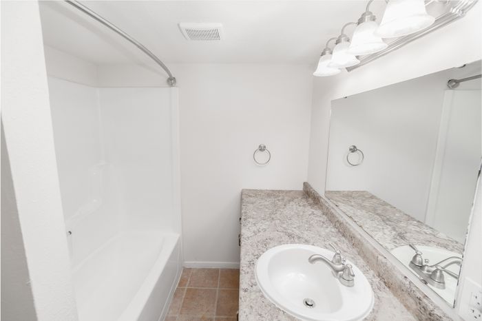 Bright and modern bathroom with elegant marble countertop, large mirror, polished chrome fixtures, and a pristine bathtub.