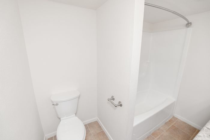 Bright and modern bathroom featuring sleek white walls, a comfortable toilet, and a pristine bathtub with a stylish curved shower rod.
