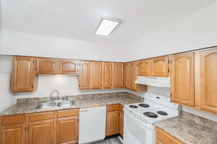Kitchen with wood cabinets, laminate countertops, electric range, dishwasher, and double sink at Lombard Heights Apartments.
