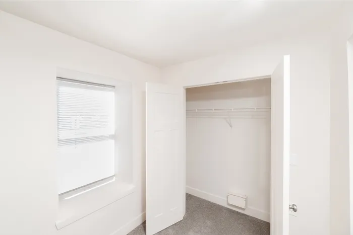 Bright and airy walk-in closet with a window offering natural light, featuring clean white walls and ample shelving spaceBedroom with window, natural light, and open closet with hanging rod at Lombard Heights Apartments.