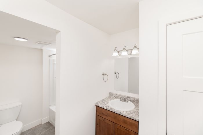 Bathroom vanity with wood cabinet, granite-style countertop, mirror, and overhead lighting at Lombard Heights Apartments.