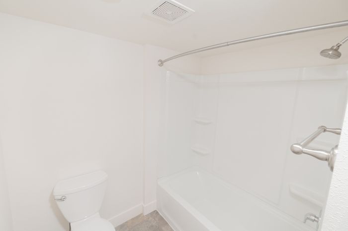 Bathroom with white tub and shower combination, curved shower rod, and toilet at Lombard Heights Apartments.