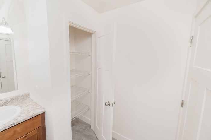 Bathroom linen closet with white wire shelving and door, located next to vanity at Lombard Heights Apartments.