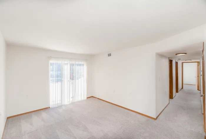 Bright and inviting apartment interior featuring plush carpeting, spacious hallway, and a sunlit room with large sliding glass doors.