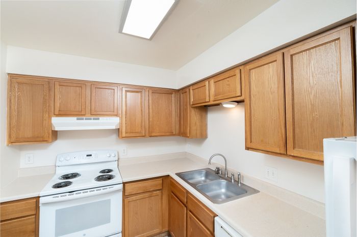 Modern kitchen with sleek wooden cabinets, dual sink, and pristine white appliances for an inviting culinary experience.