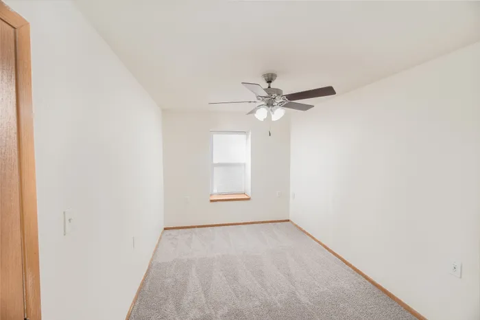 Bright and cozy room with soft carpet flooring and a ceiling fan, perfect for comfort and relaxation.