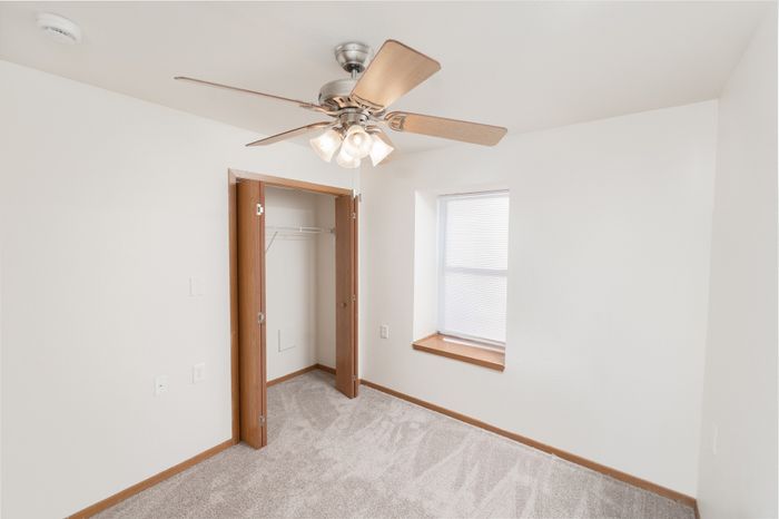 Bright and inviting bedroom featuring plush carpeting, a ceiling fan for comfort, and a spacious closet with stylish wooden doors.