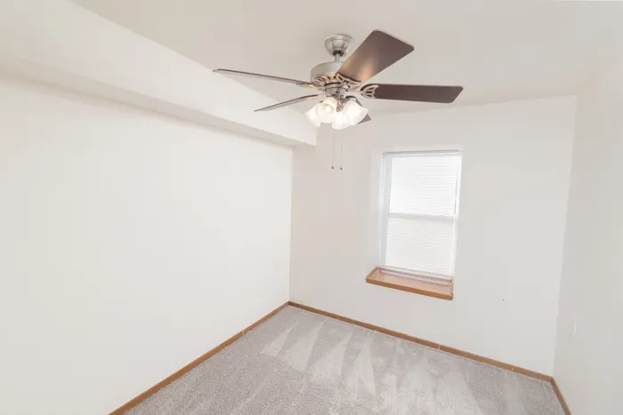 Bright and airy room featuring a modern ceiling fan, plush carpeting, and a large window for natural light.