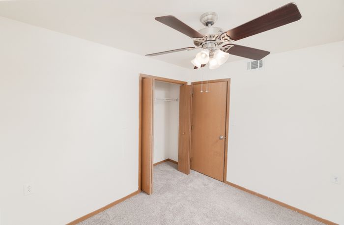 Cozy bedroom with plush carpet, modern ceiling fan, and ample closet space, perfect for comfortable living.