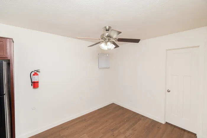 Open living and dining area with ceiling fan, wood-style floors, white walls, and interior door access.