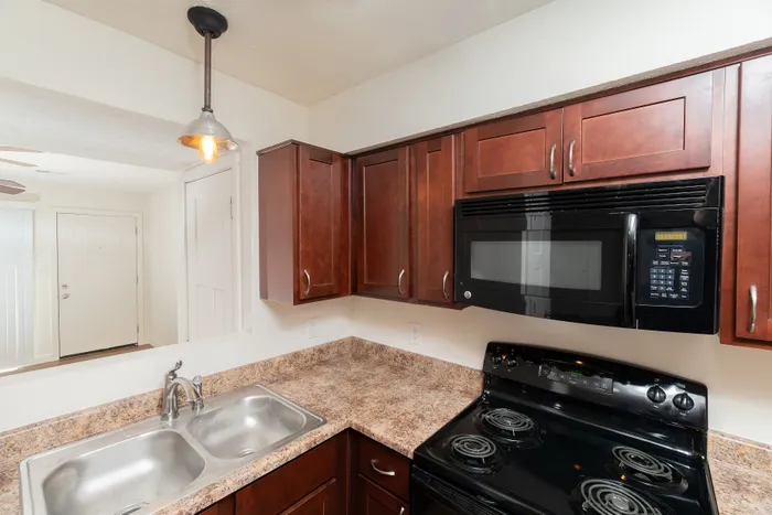 Kitchen with dark wood cabinets, laminate countertops, black appliances, and window above counter.