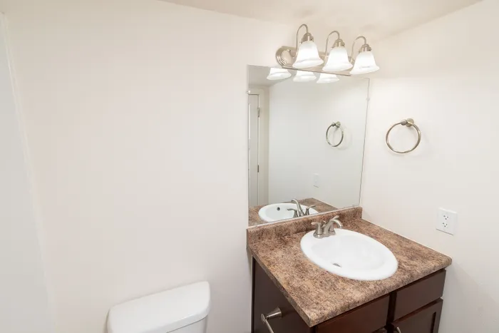 Bathroom vanity with laminate countertop, single sink, wall mirror, and brushed-nickel lighting.