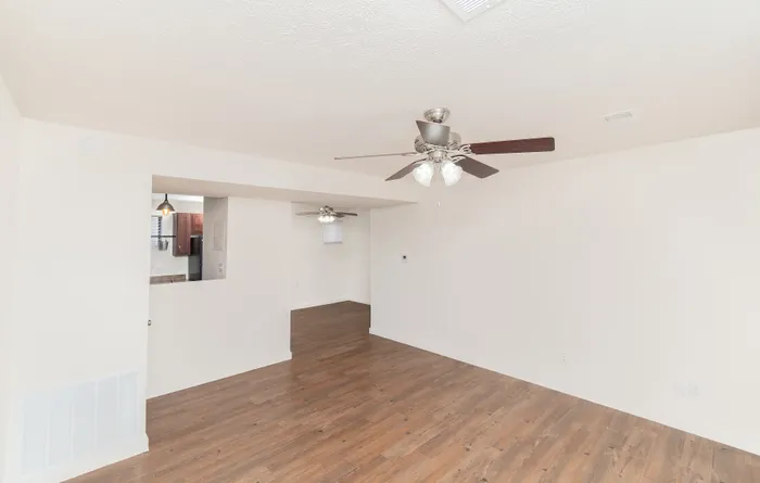 Open living area with wood-style flooring, ceiling fan, and kitchen pass-through view.
