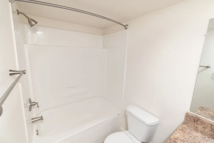 Bathroom with white tub and shower combo, curved shower rod, toilet, and neutral walls.