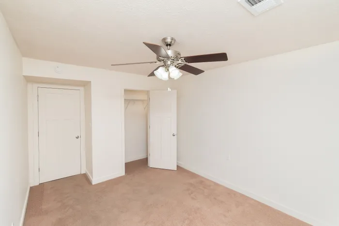 Carpeted bedroom with ceiling fan, closet access, and neutral walls.