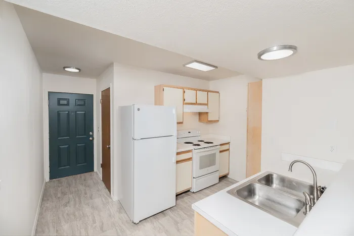 Kitchen with white appliances, light cabinetry, breakfast bar, wood-look flooring and entry door view