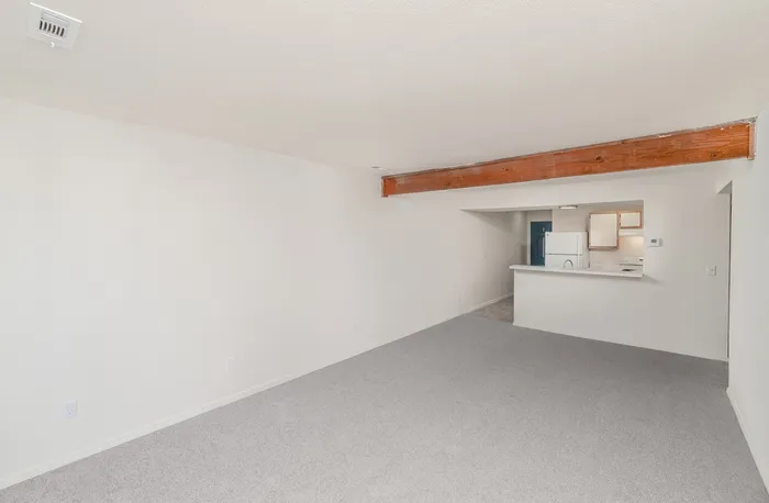 Spacious open living area with neutral carpet, kitchen breakfast bar and exposed ceiling beam