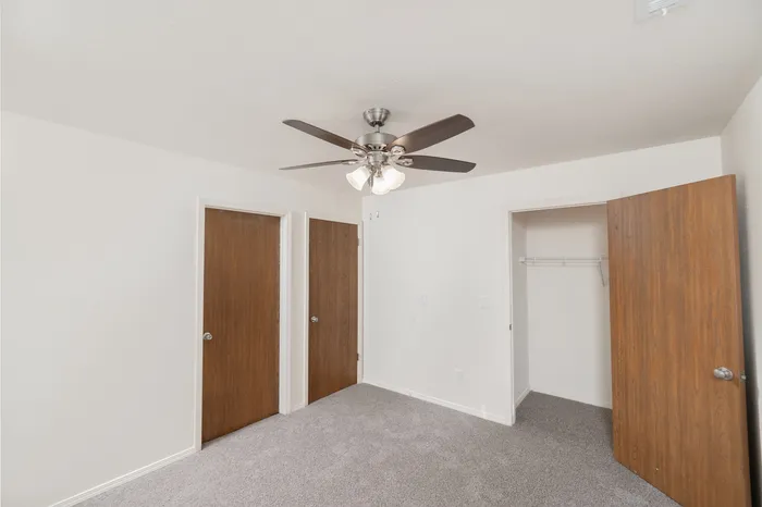 Bedroom with closet, neutral carpet, ceiling fan and wood-tone interior doors