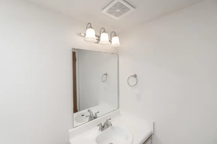 Bathroom vanity with mirror, overhead lighting, white countertop and modern fixtures