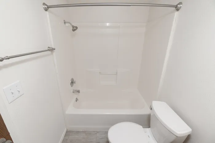 Full bathroom with tub/shower combo, white surround, toilet and towel bar