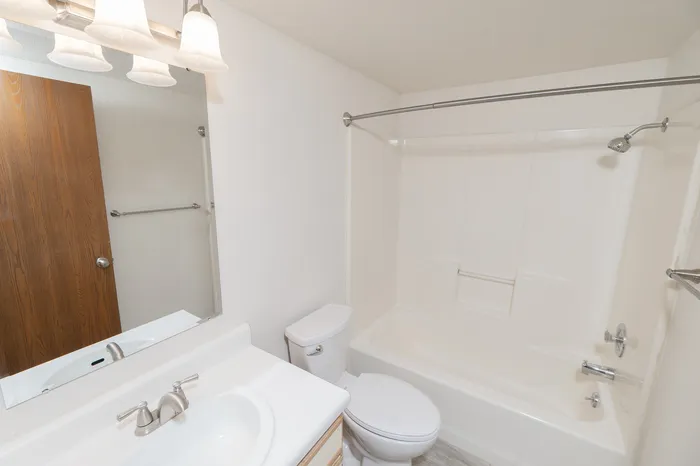 Bathroom with vanity sink, mirror lighting, toilet and tub/shower combo with white surround