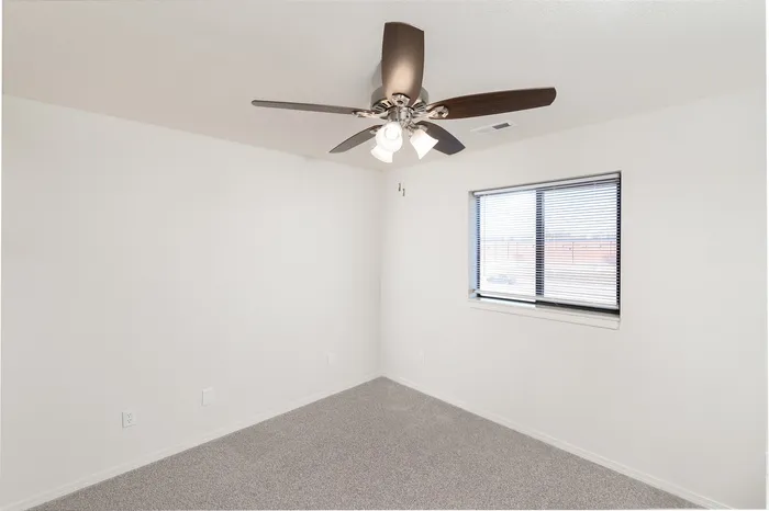 Bedroom with neutral carpet, ceiling fan with light fixture, window with blinds and clean wall space