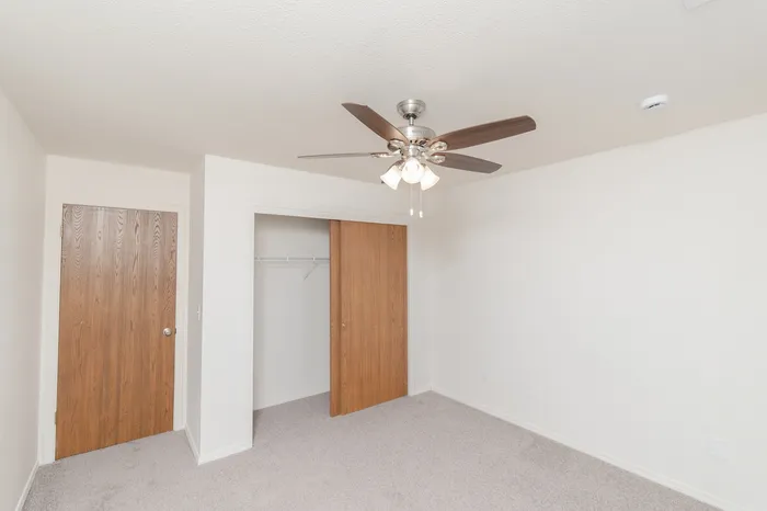 Bedroom with ceiling fan, neutral carpet, closet with sliding doors and wood-tone interior doors