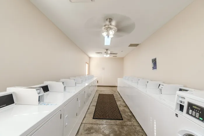 Spacious laundry room with rows of modern white washing machines and dryers, featuring a clean and bright environment.