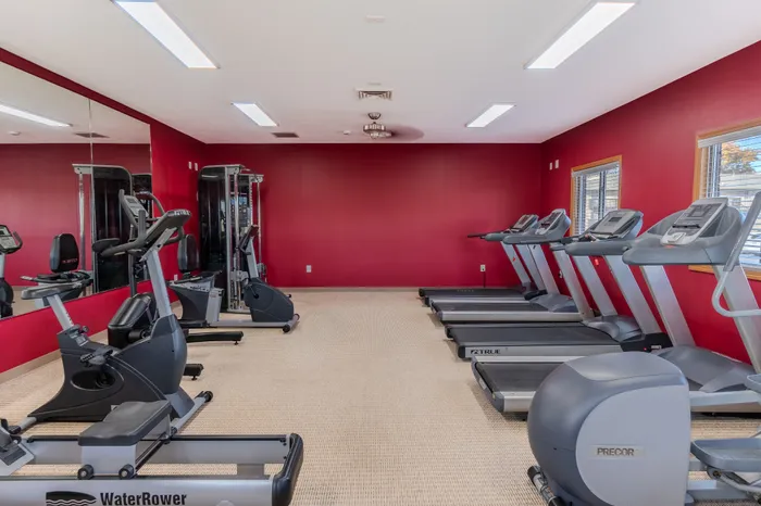 Bright and modern fitness center with red accent walls, featuring state-of-the-art treadmills, exercise bikes, and strength training equipment.