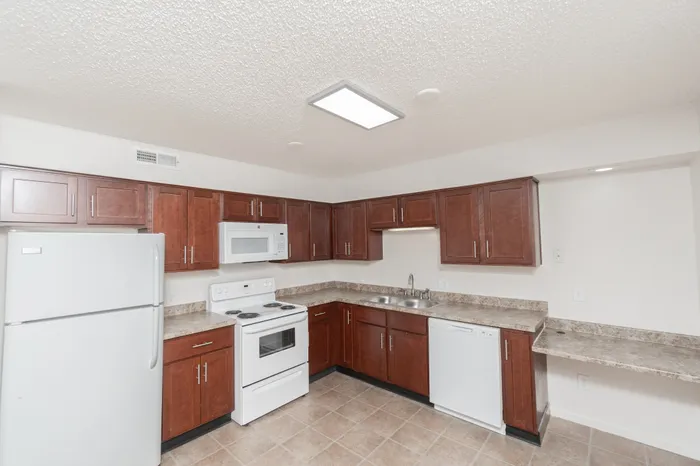 Kitchen with brown cabinets, white appliances, tile flooring, and breakfast bar at Quail Ridge East Apartments.